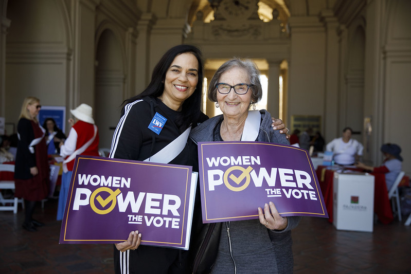 Two women holding signs saying "Women Power the Vote"