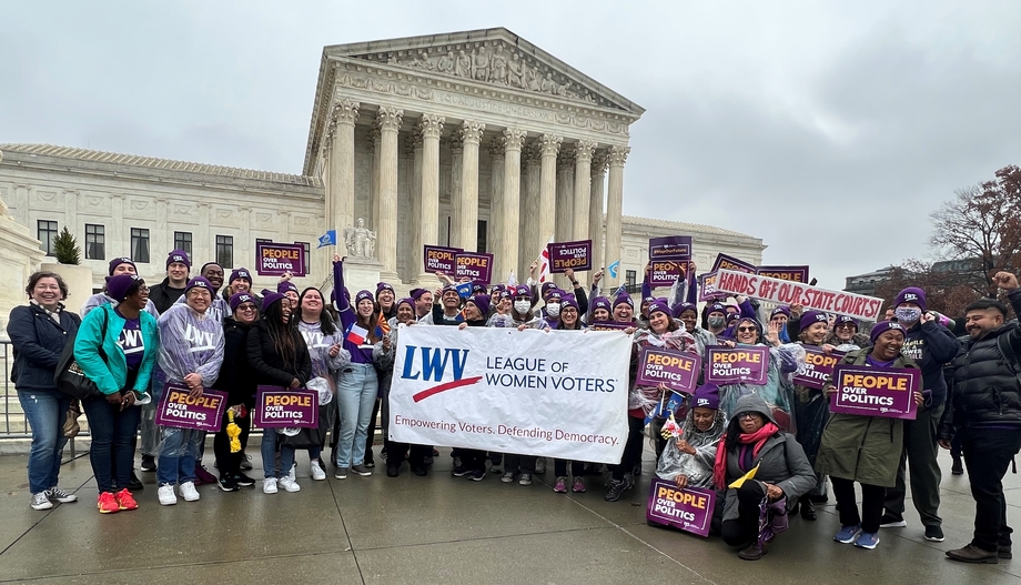 Large group of people holding a banner depicting the League of Women Voters logo standing in front of the US Supreme Court