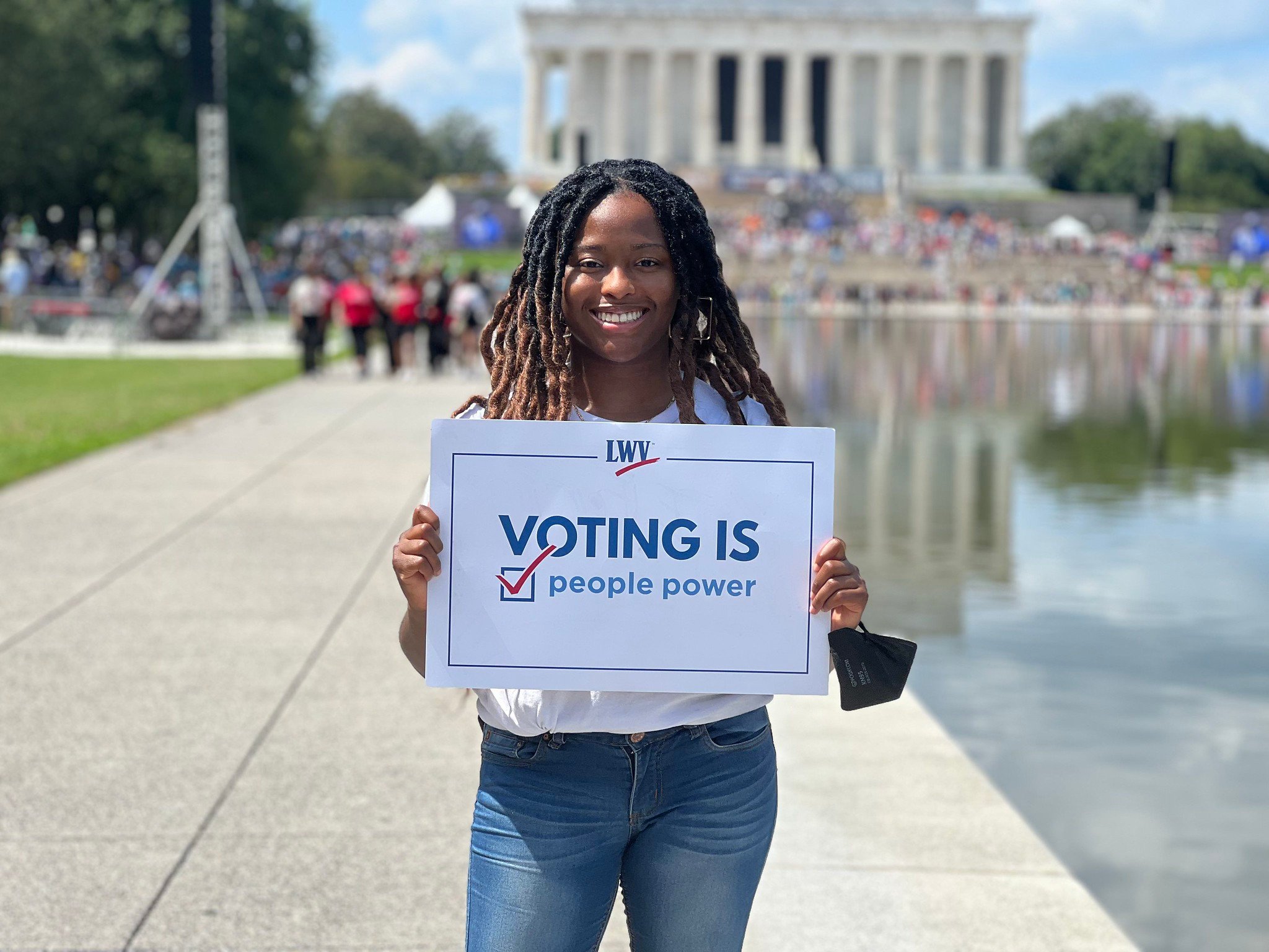 A League member by the DC Reflecting Pool holding a sign that says "Voting is People Power"