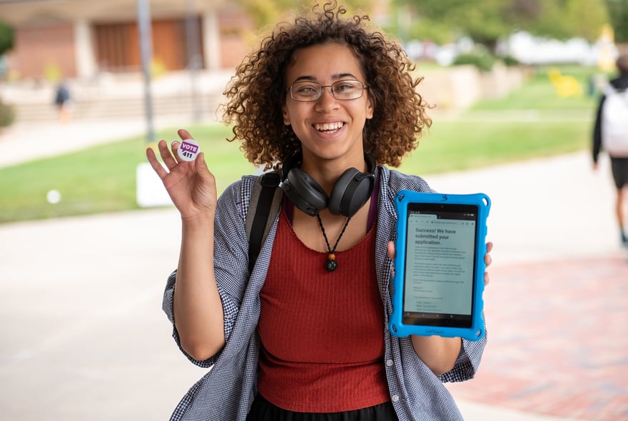 A young girl holding a VOTE411 pin and a voter registration tablet