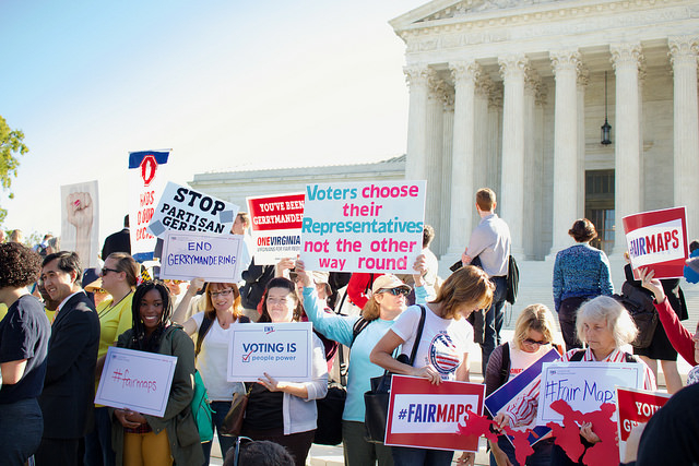 Rally participants stand in front of the Supreme Court with signs demanding fair maps