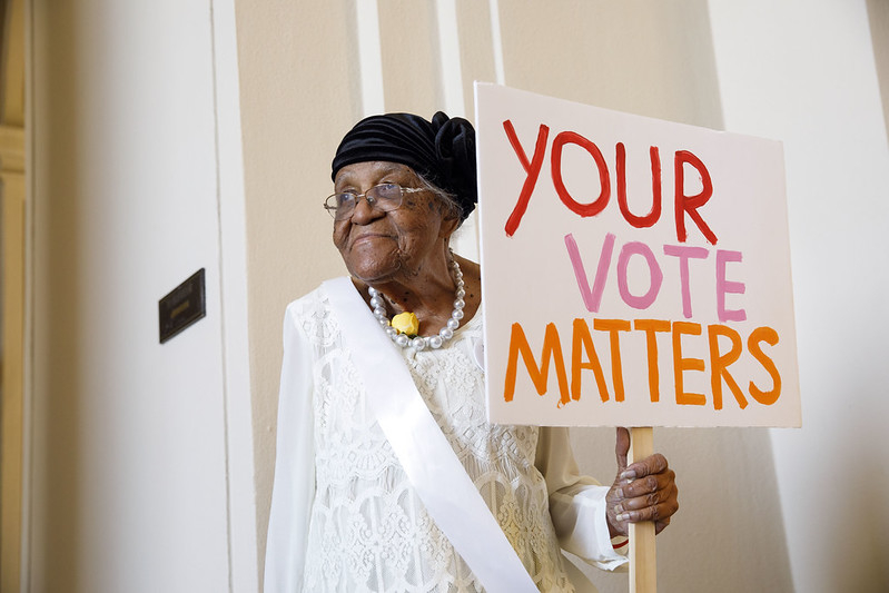 An elderly woman holding a sign that says 