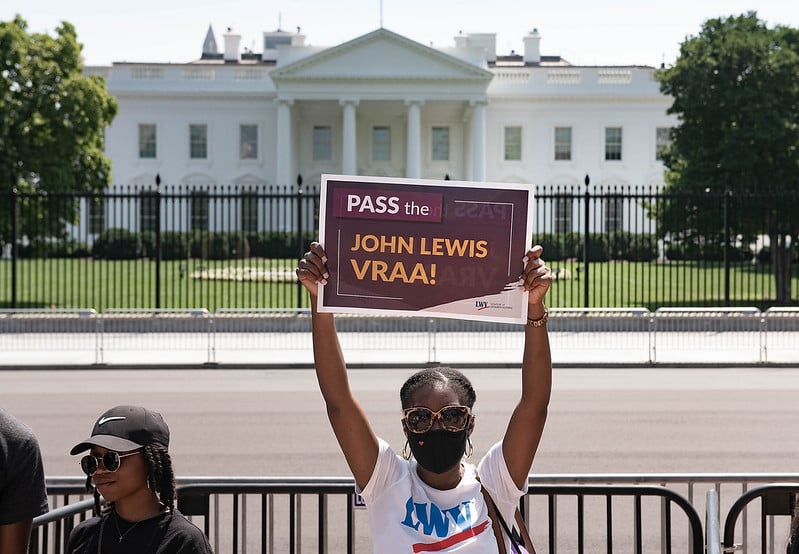 A woman in a LWV T-shirt in front of the White House holding a sign that says 