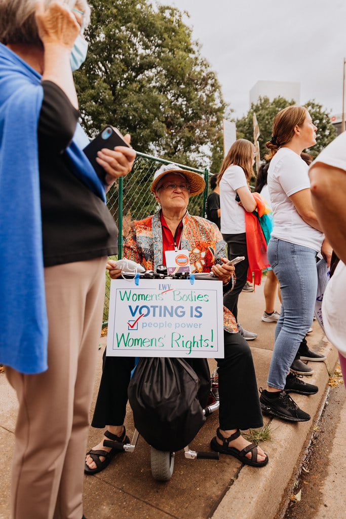 An LWV member in a wheelchair holding a sign that says 