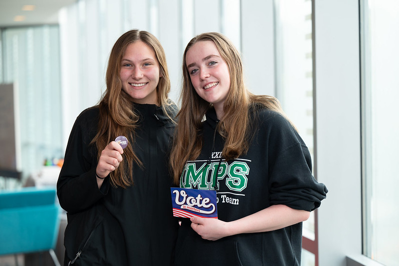 Two young women, one holding a Women Power Democracy button