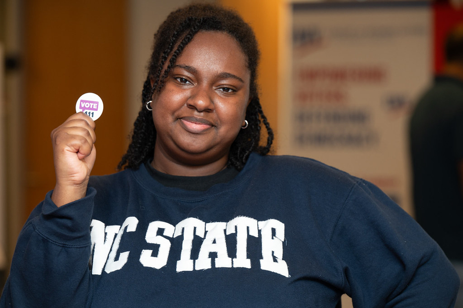 A young woman holding up a VOTE411 button