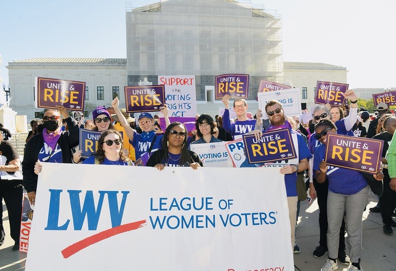 League staff holding a League of Women Voters banner in front of the Supreme Court