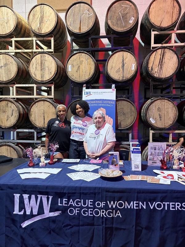 Two people at a LWV table in front of various brewery kegs.