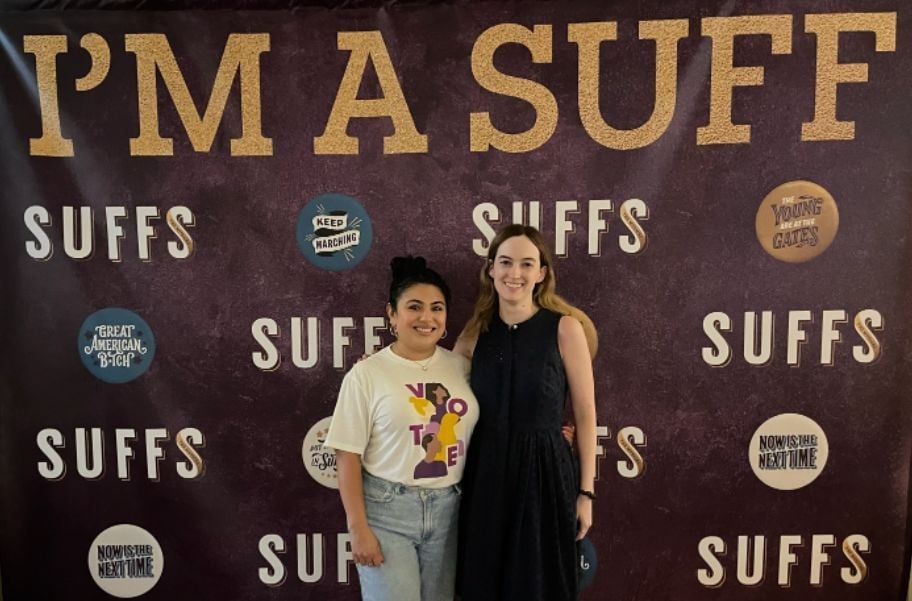 Two League members in front of a SUffs step and repeat