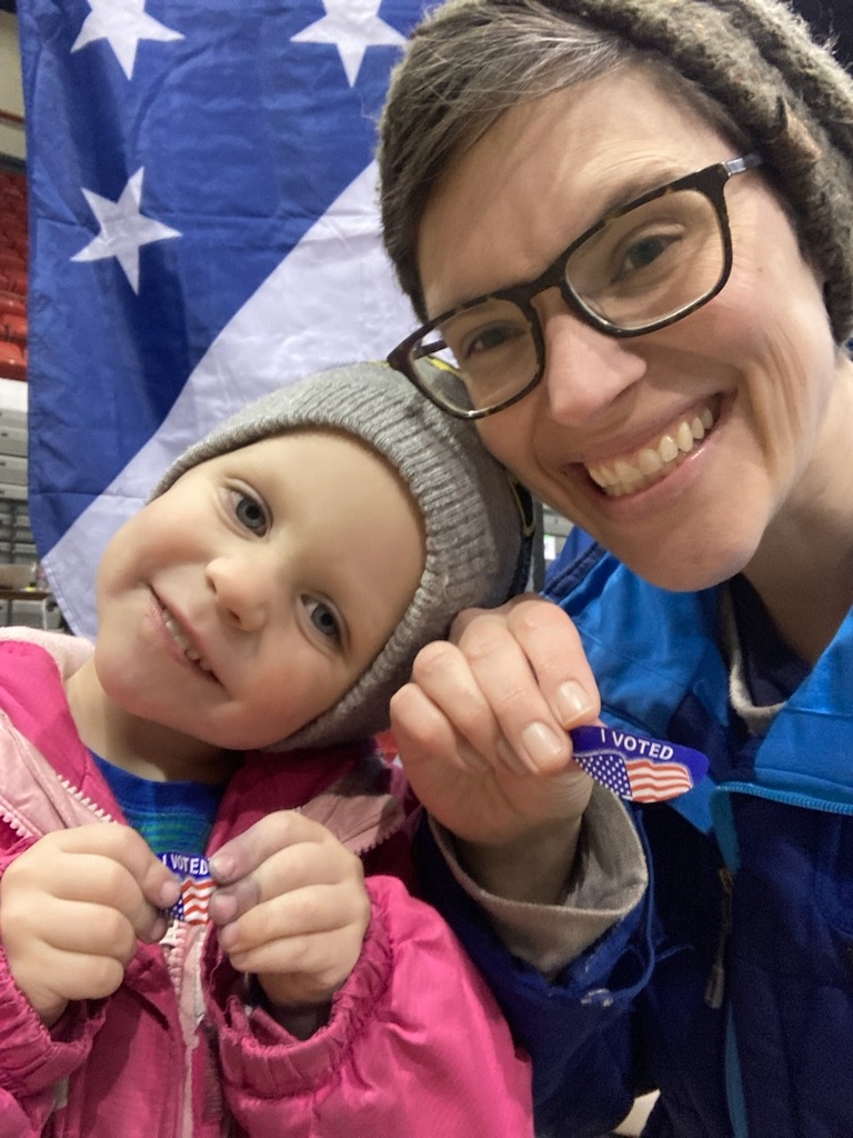 LWV employee and her child holding up "I Voted" stickers in front of an American flag