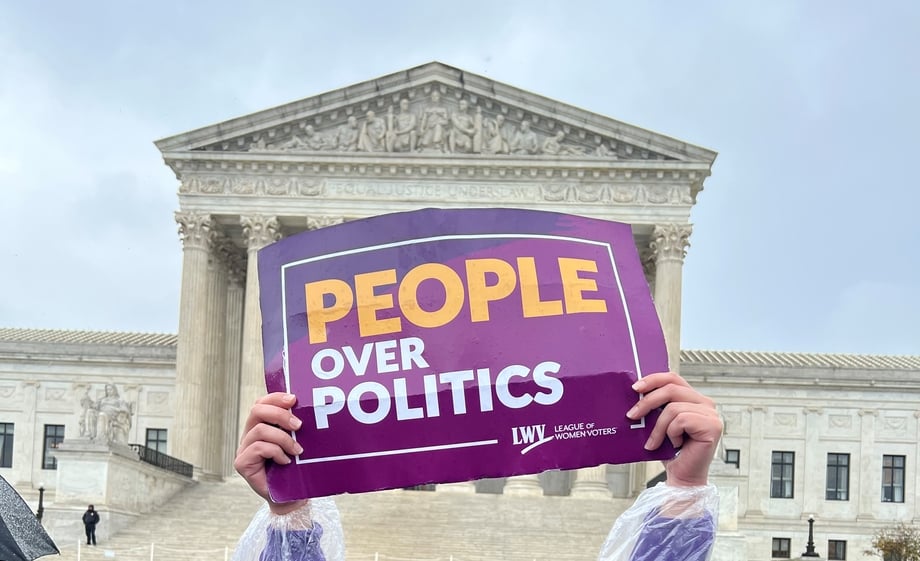 Hands holding purple and gold sign that reads 