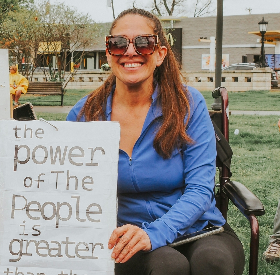 A smiling woman in a wheelchair holding a sign that says 