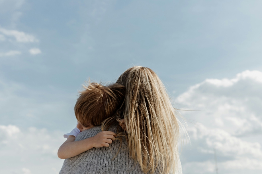 A blonde woman holding a child and looking away from camera at the blue sky