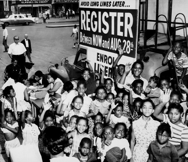 A black and white photo of children sitting in front of a voter registration sign