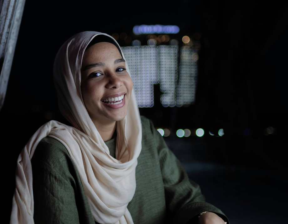 A girl sitting in a window and laughing with a city at night behind her