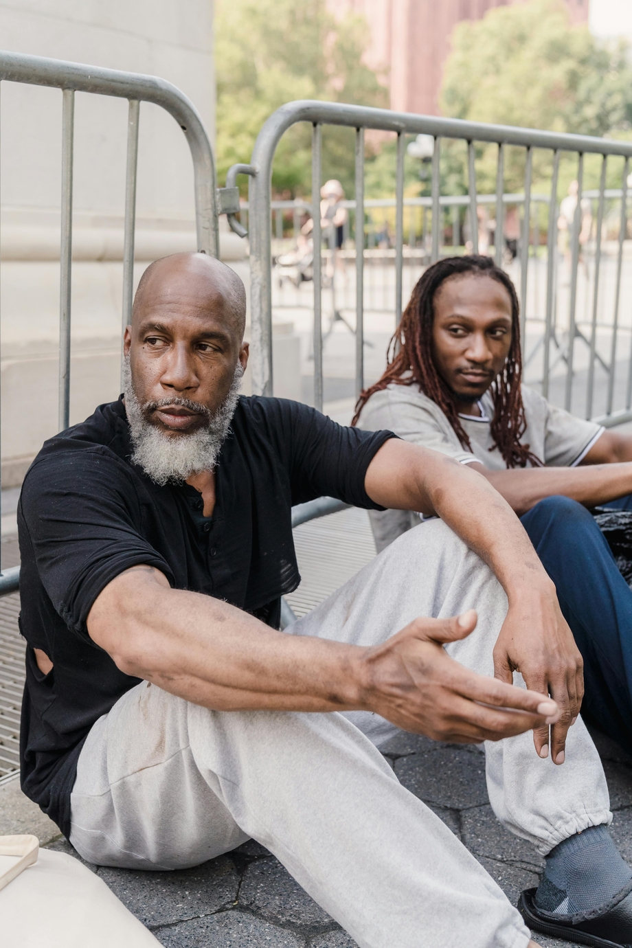 Two unhoused men sitting, leaning against a barrier